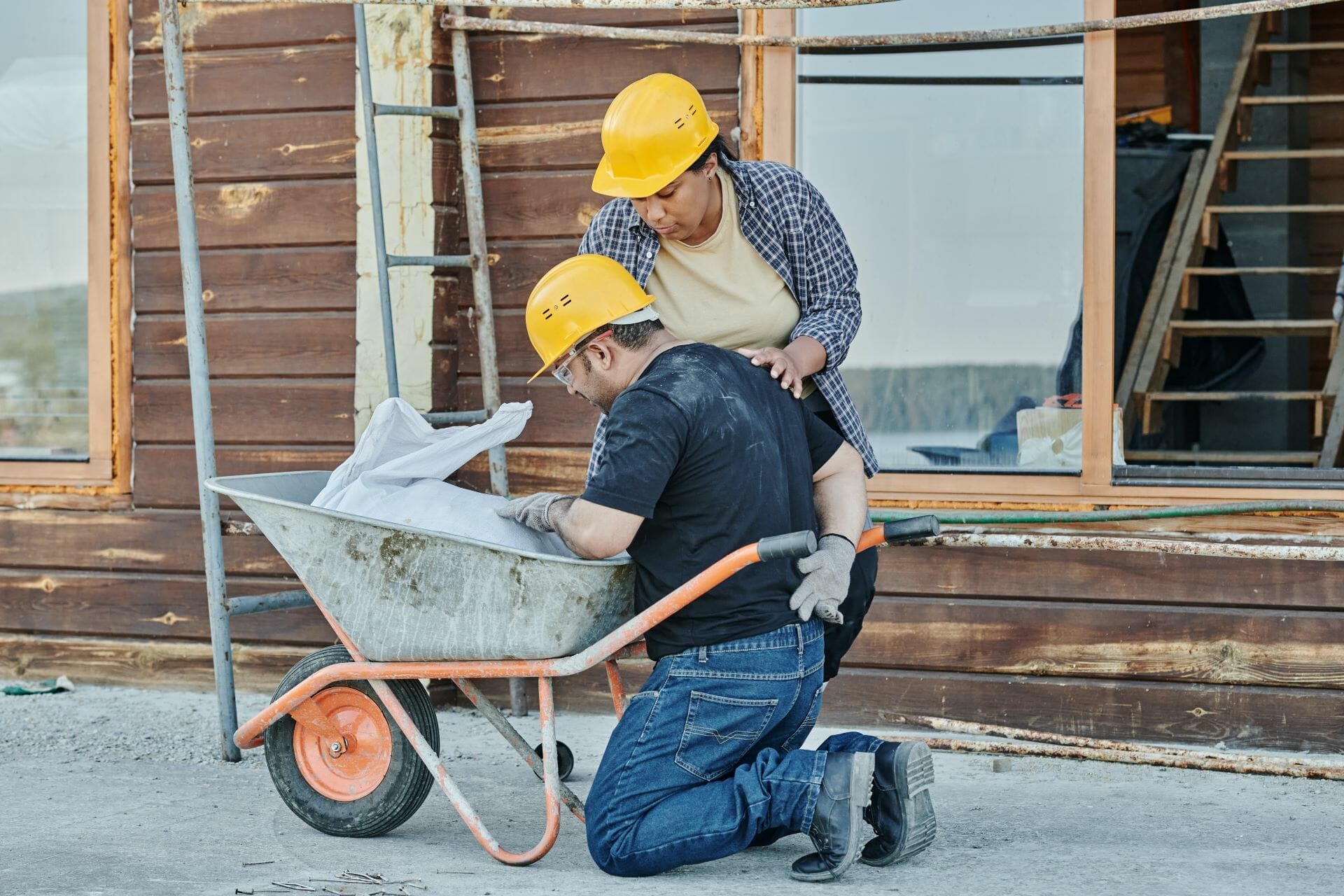 A worker on the ground behind a wheelbarrow holding their lower back after being injured from a profession with a high rate of RSI.