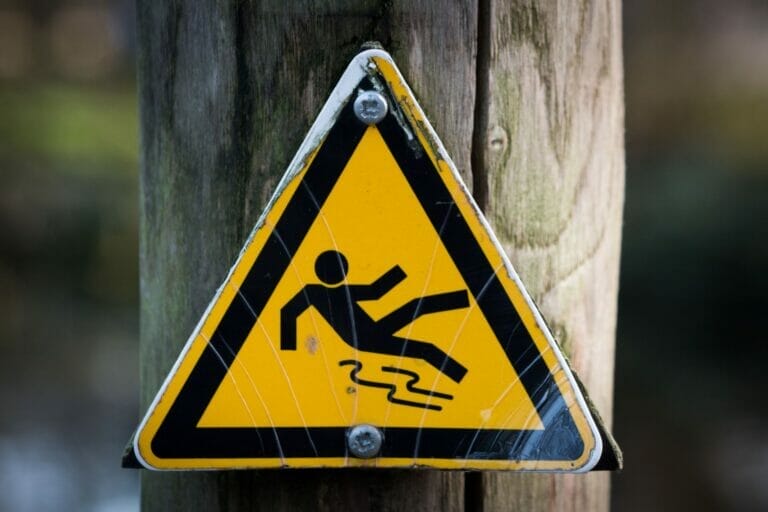 A sign on a post showing an icon to note a slip and fall risk on a premises that may also be a general liability.